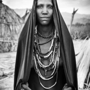 An Arbore woman stands with a beautiful black mantle draped over her head.