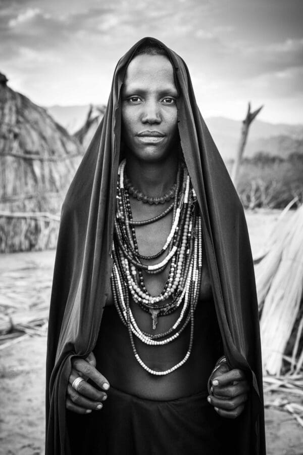 An Arbore woman stands with a beautiful black mantle draped over her head.