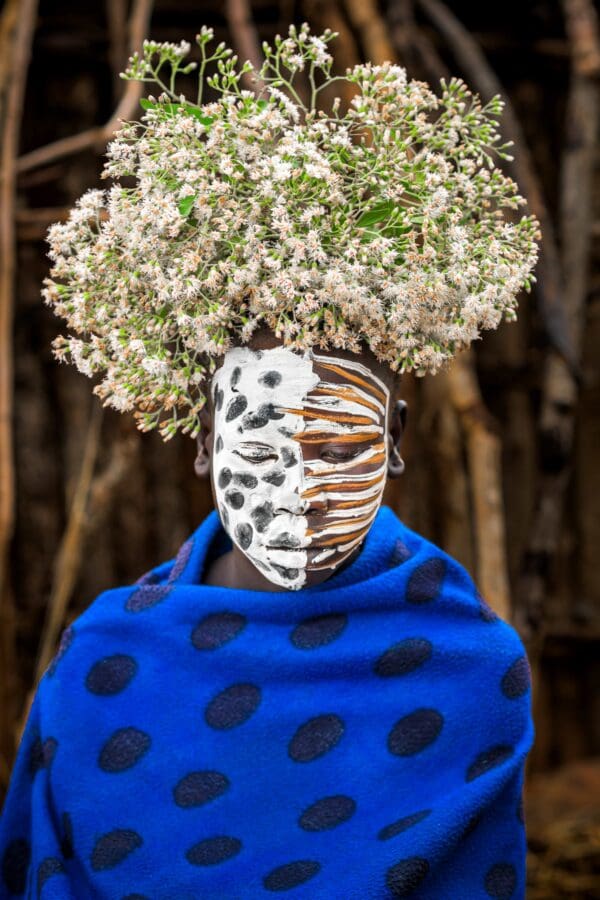 A young Suri boy wears a blue wrap with a crown of flowers on his head.