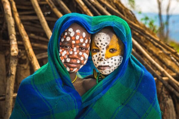 Two boys have their faces painted and are framed by a blue and green blanket