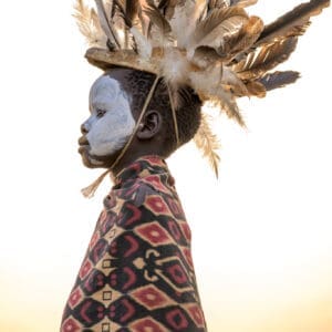 A young Suri boy wears a beautiful, feathered headdress.