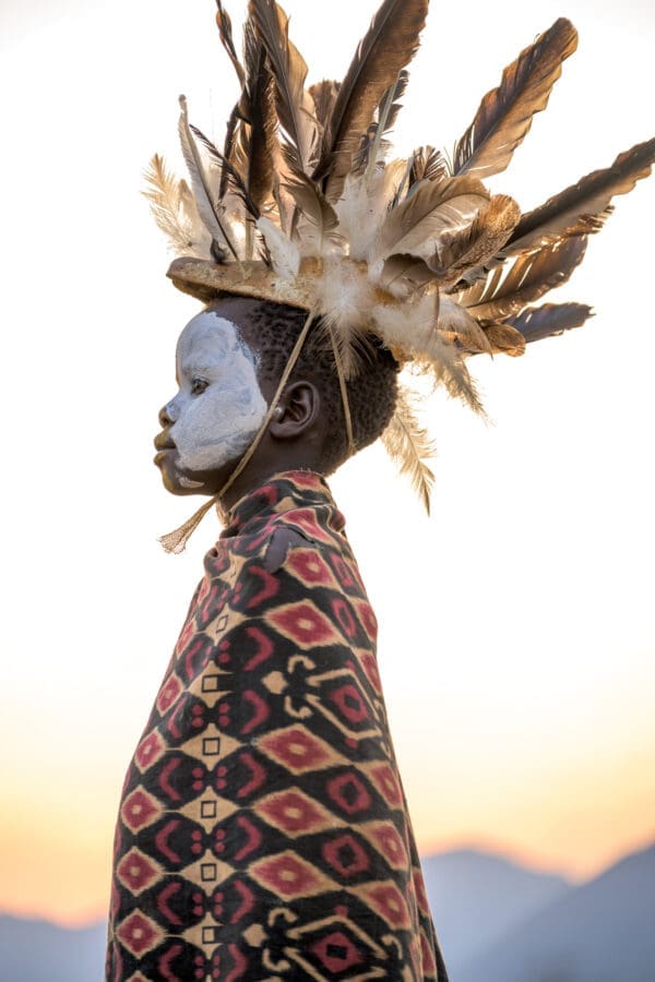 A young Suri boy wears a beautiful, feathered headdress.