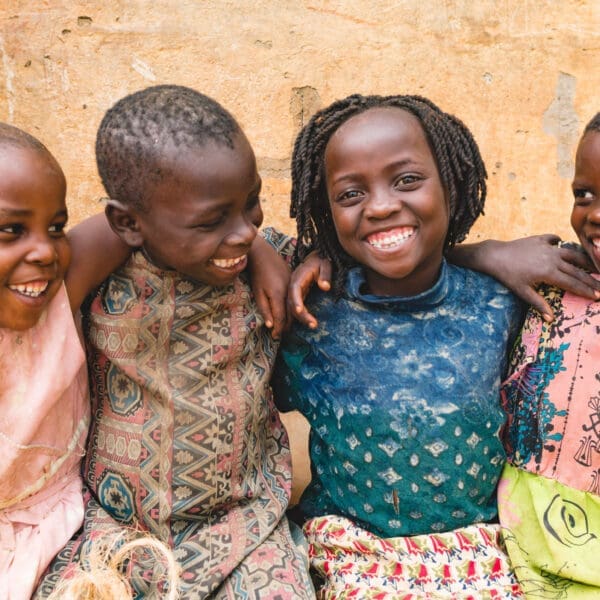 Four Ugandan children smile with their arms over their shoulders.