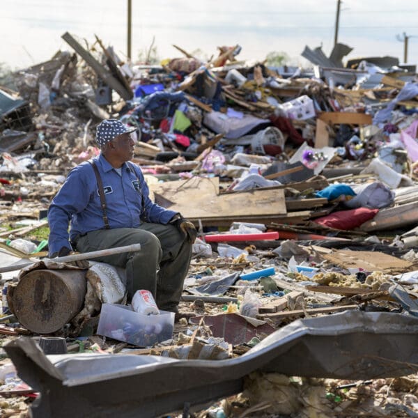 A man sits in the wreckage of where his home used to be.